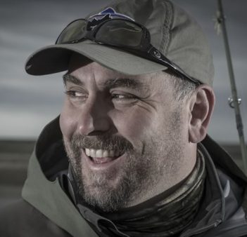 A man smiles while holding a fishing rod.