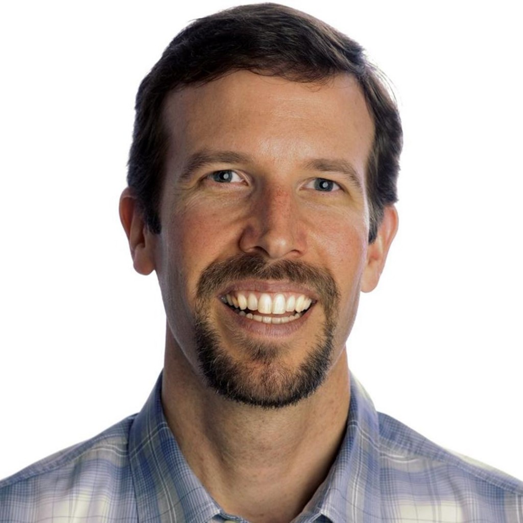 A man with a beard and a plaid shirt smiling.