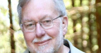 A man with glasses and a beard in front of a forest.