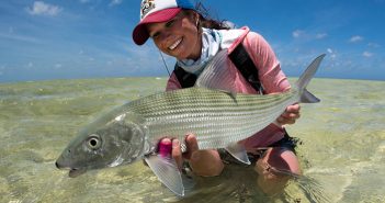 A woman holding a striped bass in the water.