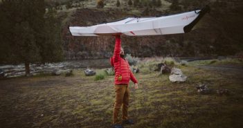 A man holding up a kayak in the middle of a field.