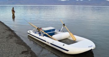 A man is standing on a small inflatable boat in the water.