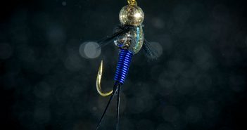 A blue and gold fishing lure hanging from a black background.