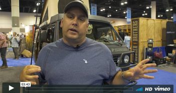 A man is standing in front of a truck at a trade show.