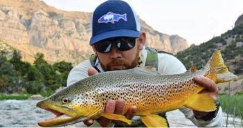 A man holding up a brown trout in a river.