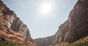 A man is paddling down a river in a canyon.