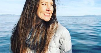 A woman smiles while standing on a boat in the ocean.