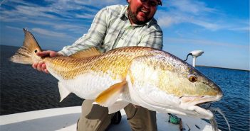 A man holding a large redfish on a boat.