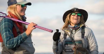 Two women wearing sunglasses and hats and holding fishing poles.