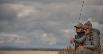 Two people sitting in a grassy area with a fishing rod.