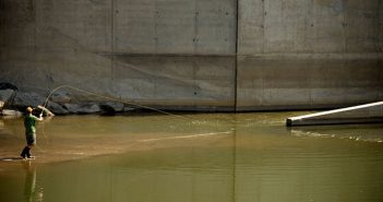 A man is fishing in the water near a concrete wall.