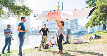 A group of people standing in a park with a kite in the air.