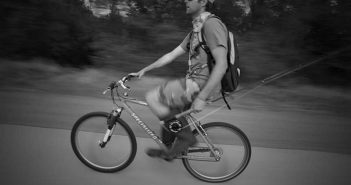 A man riding a bike with a dog on his back.