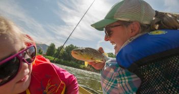 A woman is holding a brown trout on a boat.