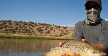 A man holding a brown trout on a river.