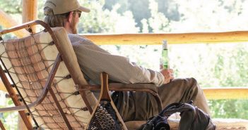 A man sits on a porch with his fishing gear.