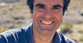 A man in a blue shirt smiling in the desert.