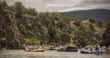 A group of people rafting down a river with cliffs in the background.