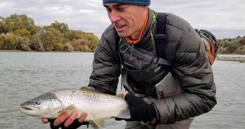 A man holding up a brown trout on a river.