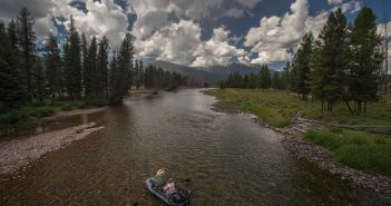 A man is fishing in a small boat on a river.