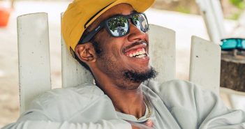 A man wearing sunglasses and a hat sitting on a beach chair.