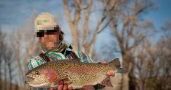 A man holding up a rainbow trout in the snow.