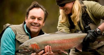 A man and woman holding up a rainbow trout.