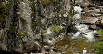 A man is standing in the middle of a rocky river.