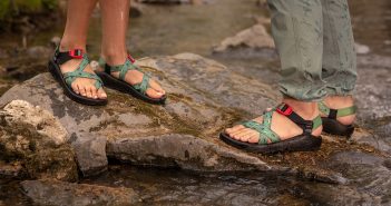 Two people standing on rocks next to a stream.