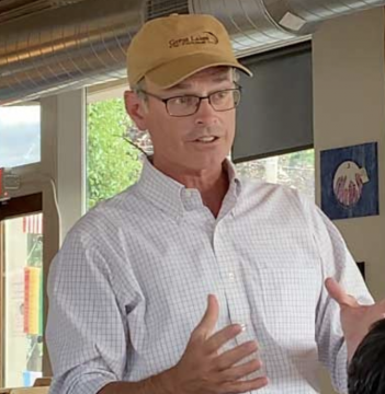 A man in a hat is speaking to a group of people.