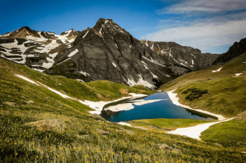 A lake in the mountains surrounded by grass and flowers.