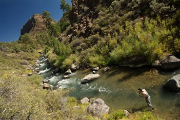 A man is fishing in a river near a rocky area.