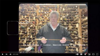 A man is holding a wooden stick in front of shelves.