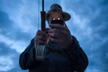 A man in a hat holding a fishing rod and a cell phone.