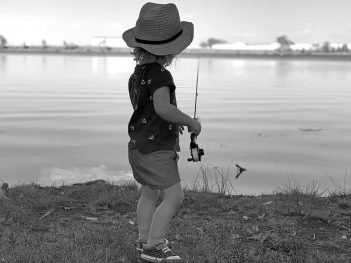 A little girl wearing a hat is standing near a body of water.