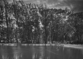 A black and white photo of a man fishing in a pond.