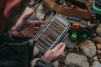 A man is holding a fly box on the ground.