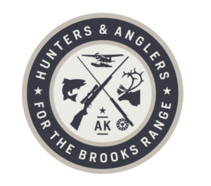 A circular logo with the text "Hunters & Anglers For The Brooks Range" surrounding images of a fish, rifle, airplane, deer head, and fishing reel, with "AK" and a star in the center.