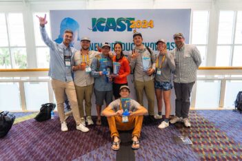 A group of eight smiling people poses in front of an "ICAST 2024" sign, holding awards and trophies, inside a well-lit room with carpeted flooring.