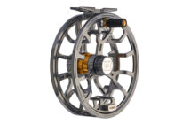 A high-quality fly fishing reel made of metal with intricate cutouts, featuring a black and gold cylindrical knob and a central logo.