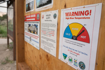 A bulletin board displays multiple notices, including a prominent poster warning about high river temperatures and their impact on fish health. Several logos and smaller notices are also visible.