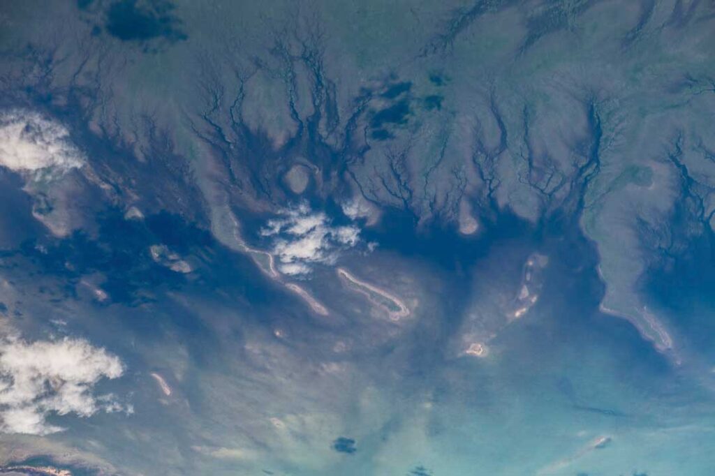 Aerial view of a river delta with branching waterways and scattered clouds, showing various shades of blue and green.