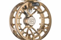 A gold-colored, intricately designed fishing reel with an open frame structure and a logo in the center.