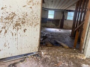 A room with dirt-splattered walls, exposed beams, and debris on the floor, viewed through an open, dirty door.