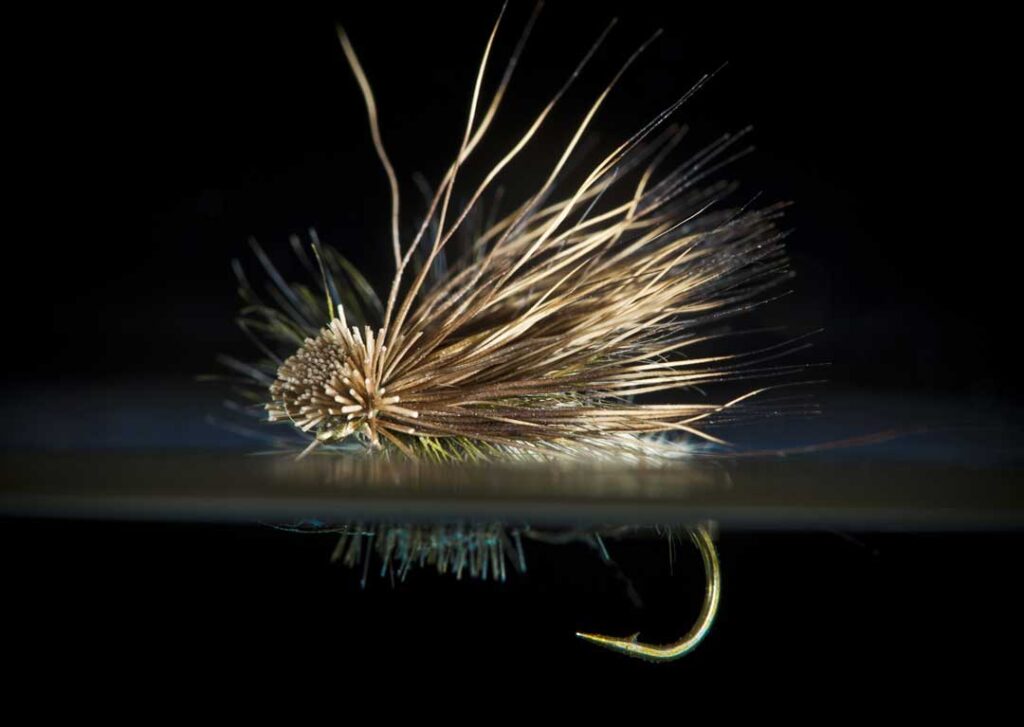 Close-up of a fishing fly with a barbed hook, featuring realistic feathery textures and intricate details, set against a dark background.