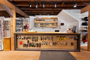 Outdoor gear store counter with display board showcasing various tools and accessories. Sunglasses and hats are on the left, and a cash register is on the right.