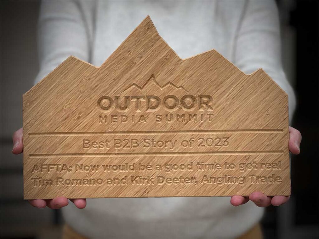 Person holding a wooden award shaped like mountains, inscribed with "Outdoor Media Summit Best B2B Story of 2023" and recipient details.