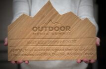 Person holding a wooden award shaped like mountains, inscribed with "Outdoor Media Summit Best B2B Story of 2023" and recipient details.