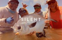 Four people holding a large fish and posing for the camera, wearing hats and sunglasses with the text "The Silent Spotter" overlaid on the image.