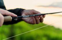 Close-up of hands holding a Sage fly fishing rod against a blurred outdoor background.